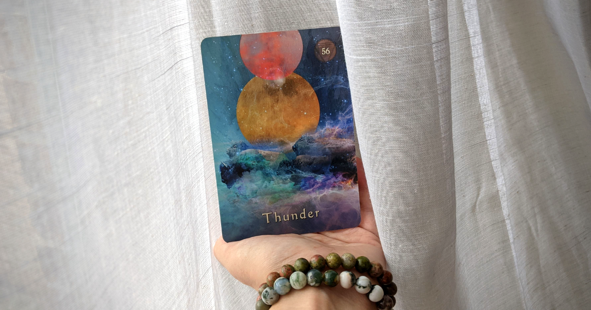An image of a hand holding a colorful card of moons and buffalo in the sky with the word Thunder