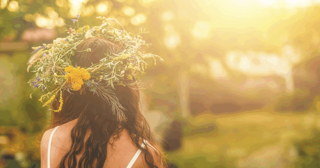 Woman with long hair wearing a crown of wildflowers standing in golden summer sunlight, symbolizing connection to nature and seasonal healing
